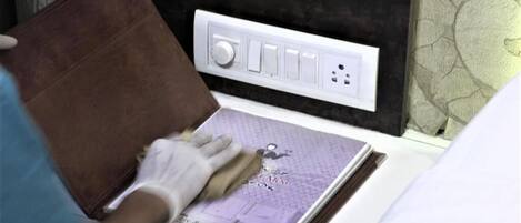 A person cleaning a leather sofa in a room with a white electrical outlet and a patterned wall.