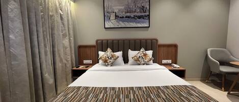 Ein Hotelzimmer mit einem großen Bett, einem Kopfteil, zwei Nachttischen mit Telefonen, einem Sessel und einem Gemälde an der Wand.