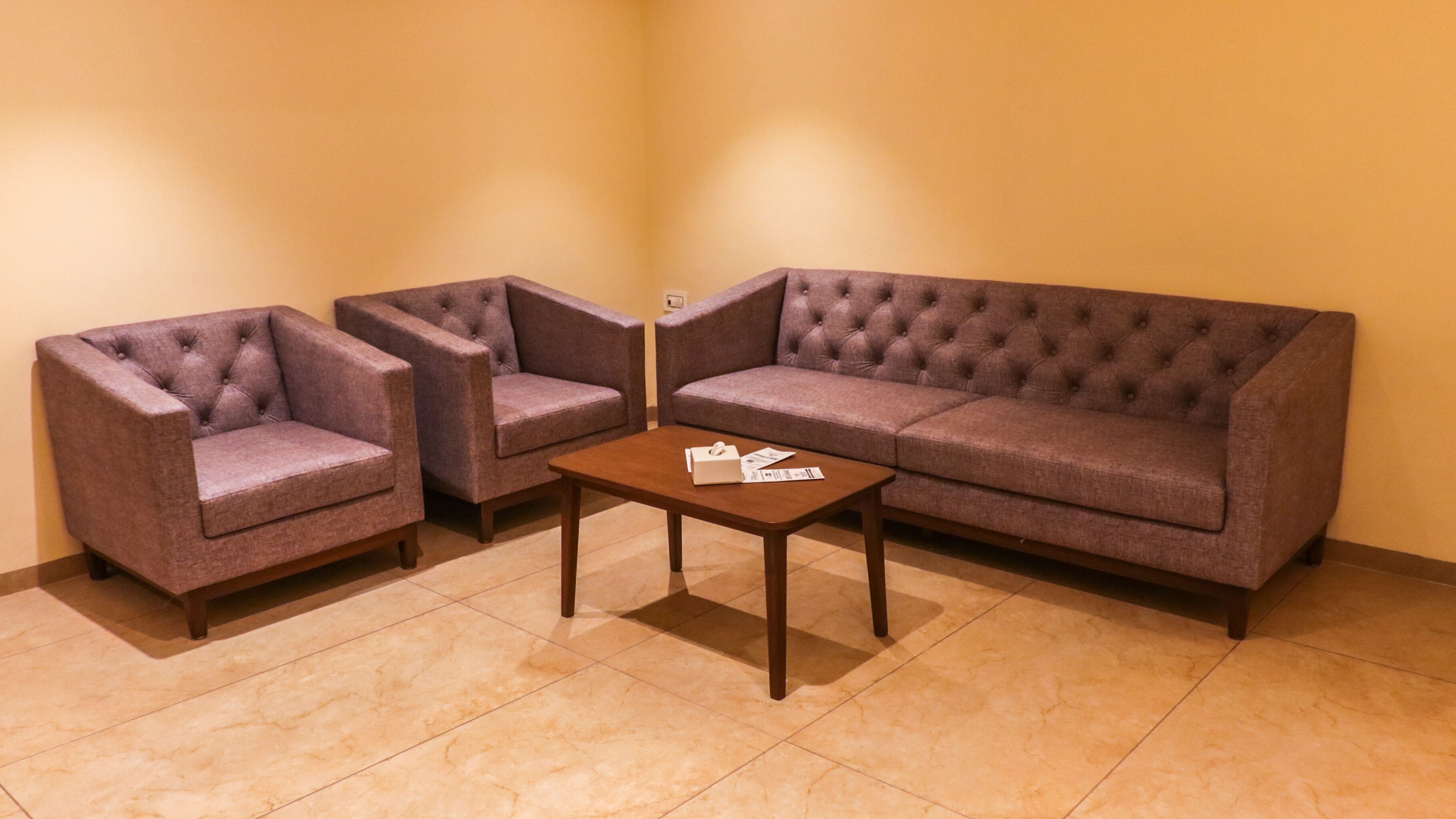 A corner room with a brown sofa, two armchairs, and a small wooden coffee table.