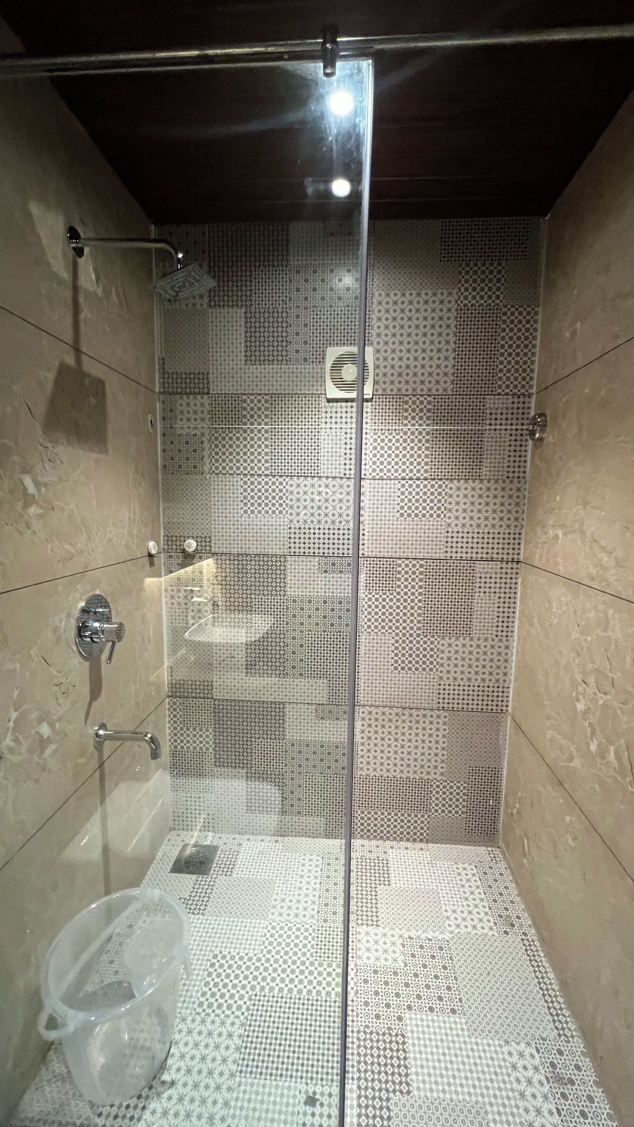 Een douche met een glazen deur, betegelde wanden en een douchekop.