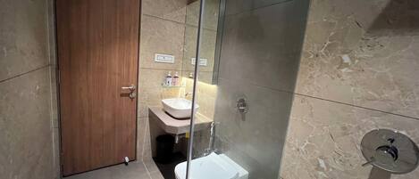 A modern bathroom with a wooden door, a glass-enclosed shower, a white sink, and a toilet.
