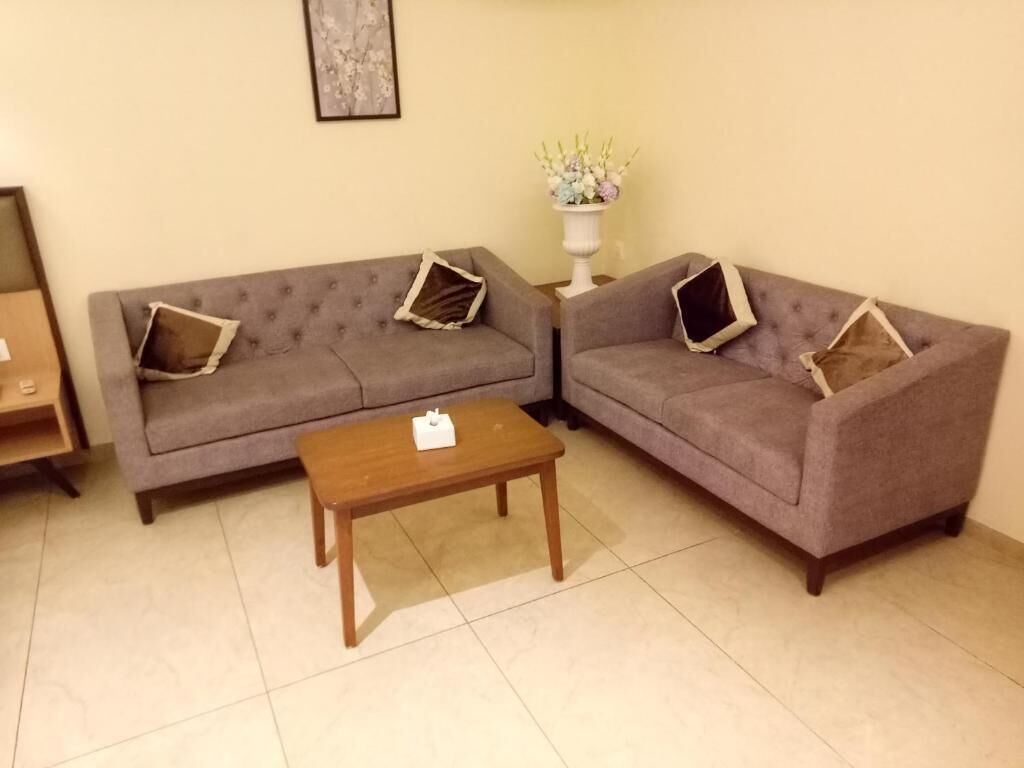 Una sala de estar con dos sofás grises, una mesa de centro de madera y un jarrón blanco con flores sobre una mesita auxiliar.