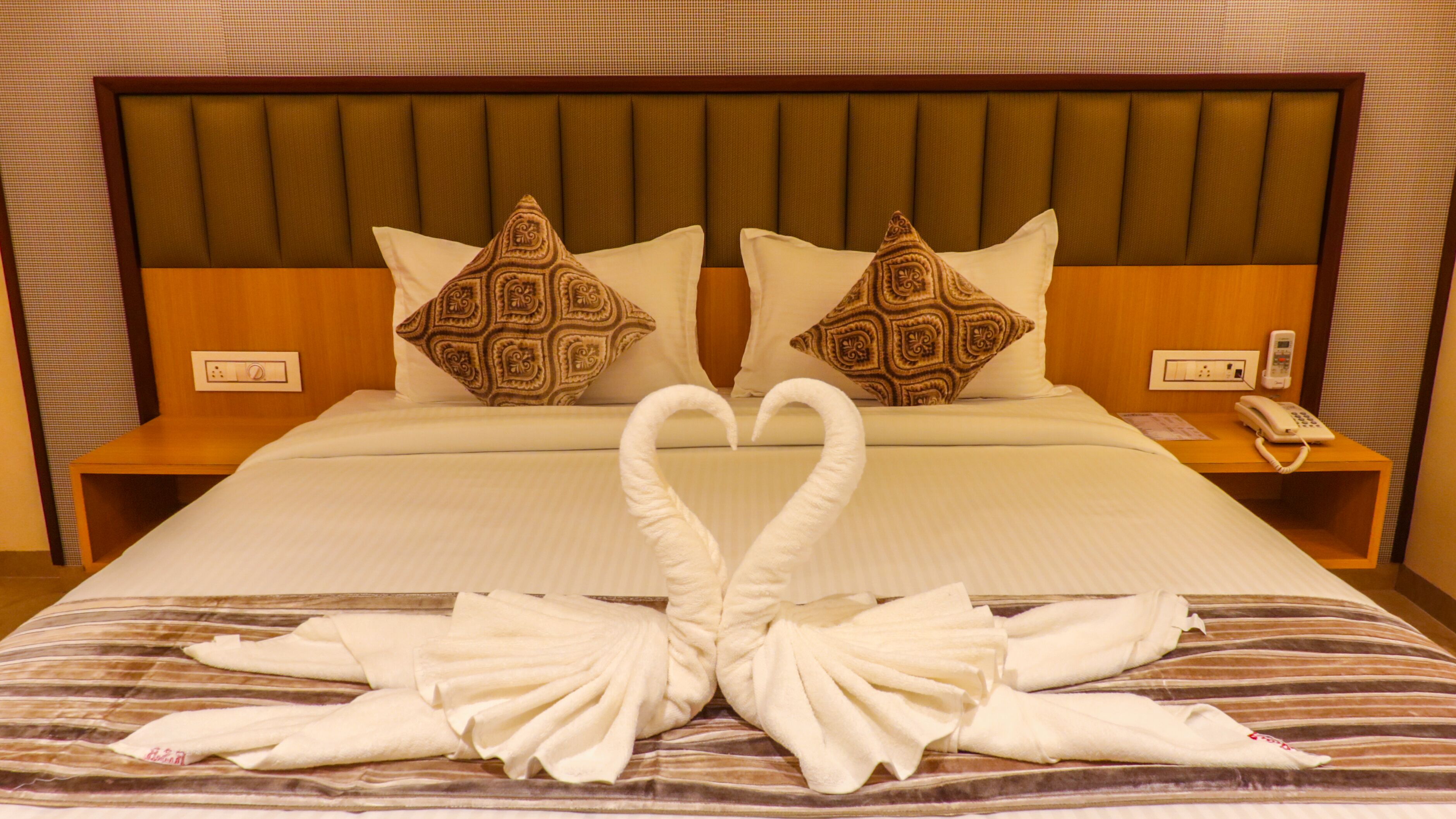 A hotel room with a large bed, two pillows, a bedside table with a phone, and a wall socket.