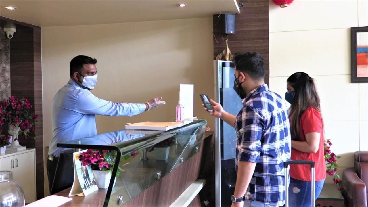 A reception area with a glass counter, a man in a light blue shirt standing behind it, and another man in a plaid shirt holding a phone.