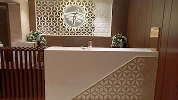 A reception desk with a geometric patterned wall, a wooden partition, and a small potted plant.