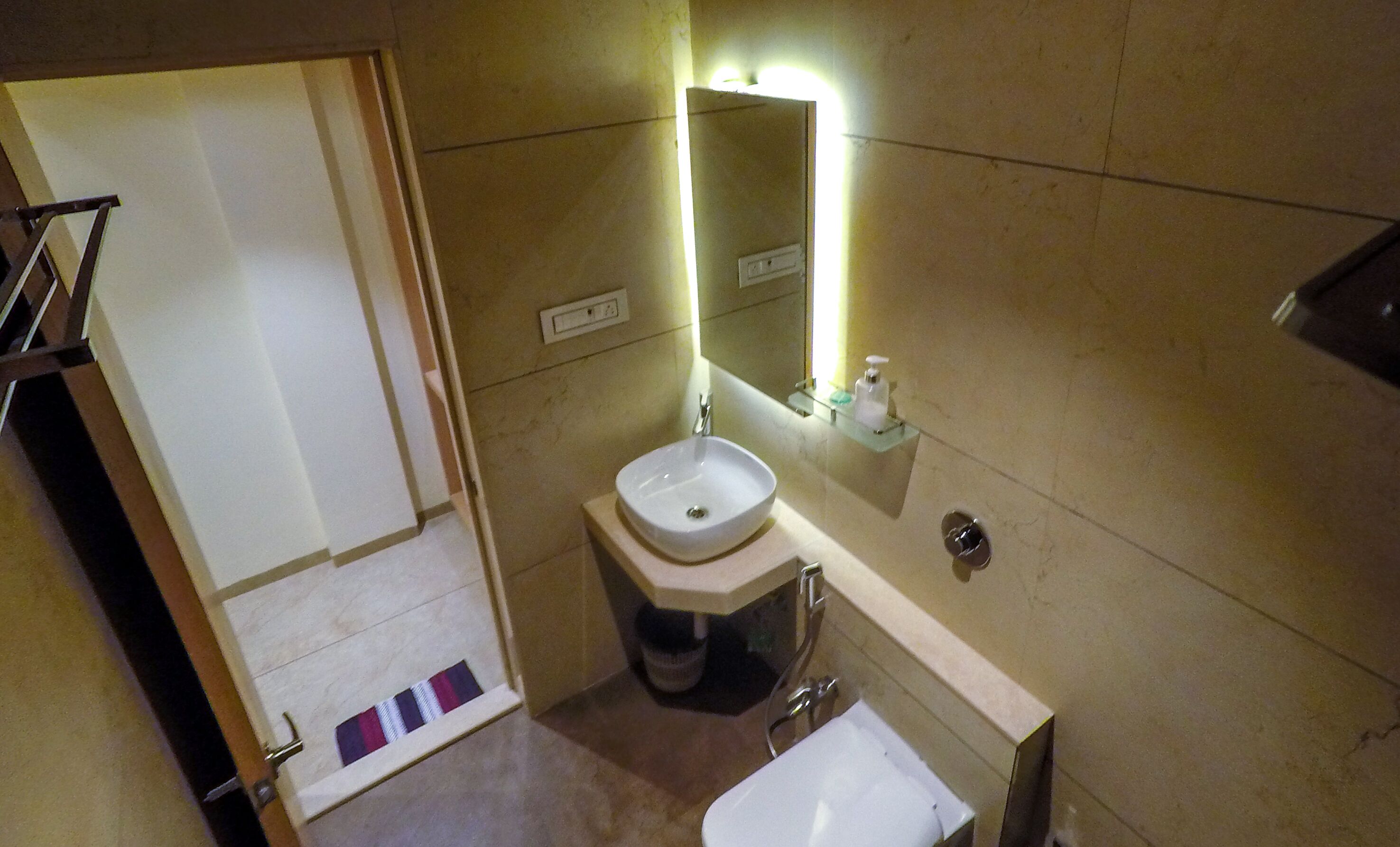 A small bathroom with a white sink, a mirror, and a toilet. There is a towel rack and a soap dispenser on the wall.