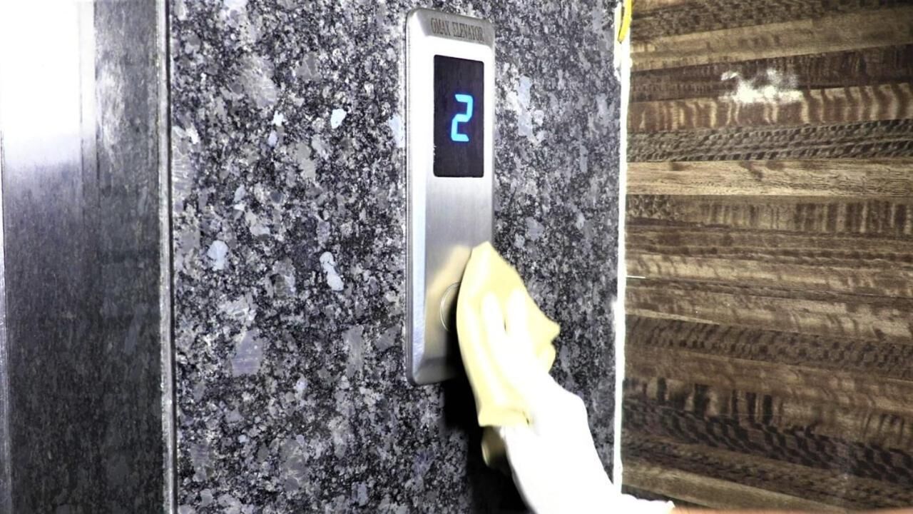 A hand pressing a button on a digital elevator control panel.