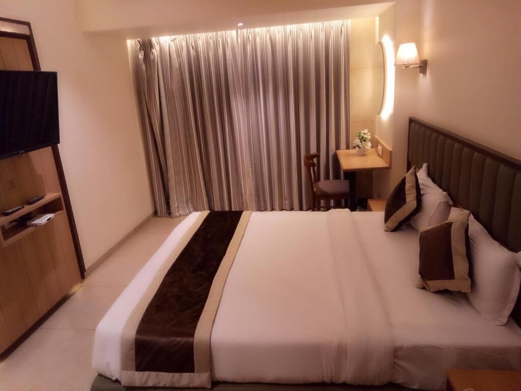 A hotel room with a large bed, a desk with a chair, a TV, and a curtain.