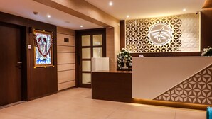 A reception area with a wooden reception desk, a decorative wall with geometric patterns, and a stained glass window. - Rudra Shelter Business Hotel (Vasai)