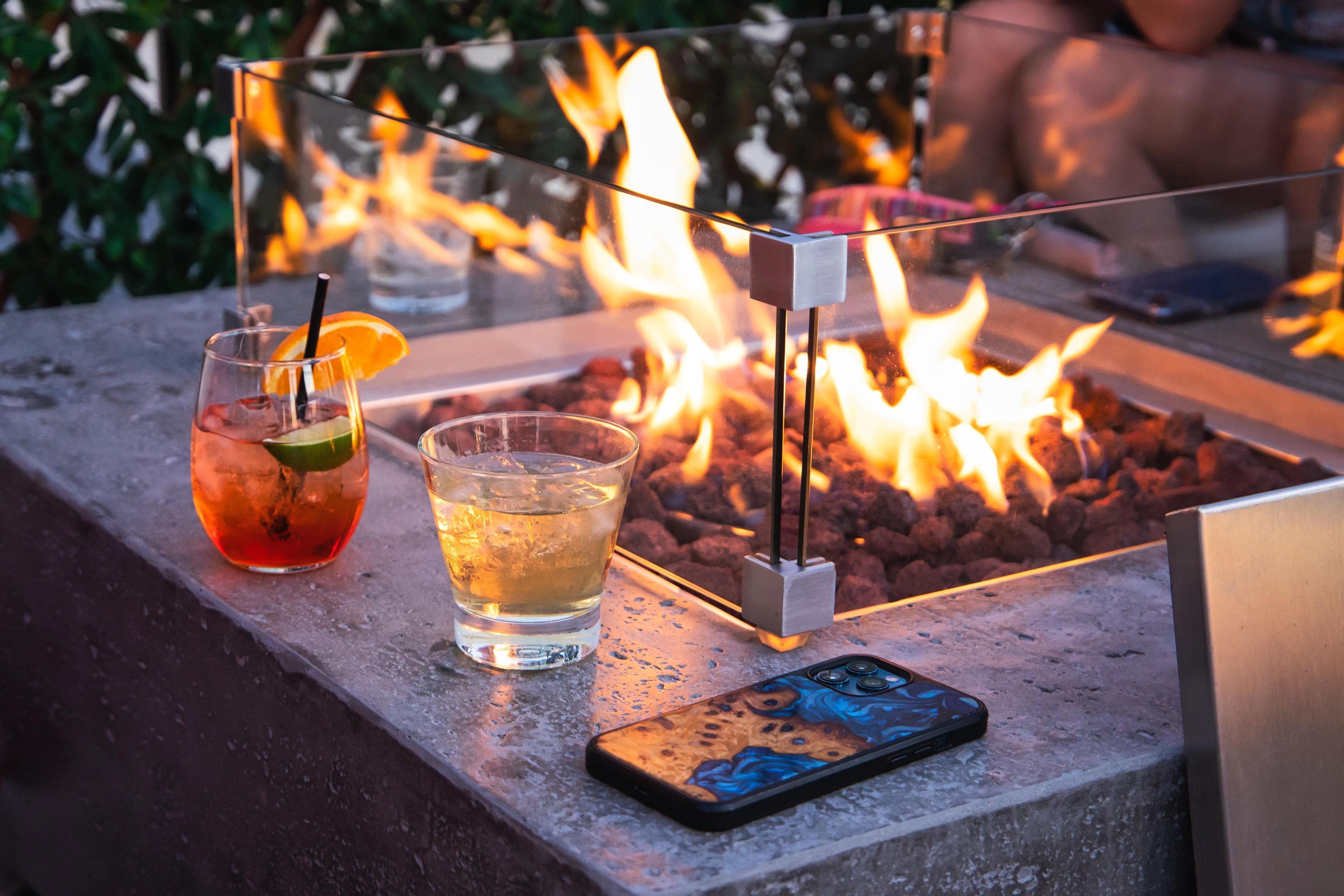 A table with two drinks, a smartphone, and a fire pit.