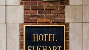 A black sign with gold lettering stating "HOTEL ELKHART" mounted on a brick wall.