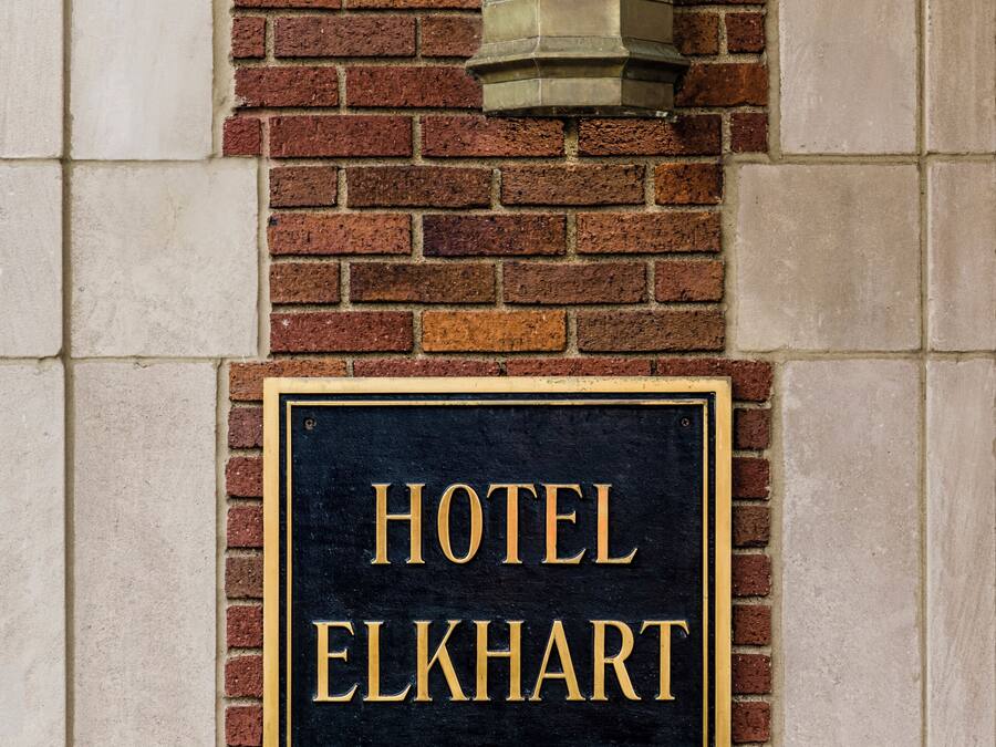 A black sign with gold lettering stating "HOTEL ELKHART" mounted on a brick wall.