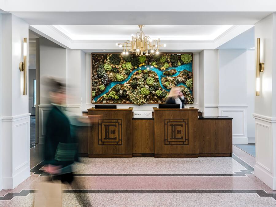 A hotel reception area with a modern chandelier, a large wall tapestry, and a reception desk.