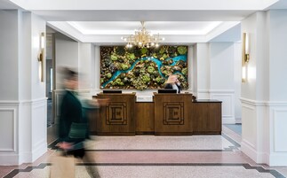 Ein Hotel-Empfangsbereich mit einem modernen Chandelier, einer großen Wandteppich und einem Empfschalter.