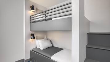 A bunk bed with a desk and chair, a small bedside table with a lamp, and a blue patterned rug.