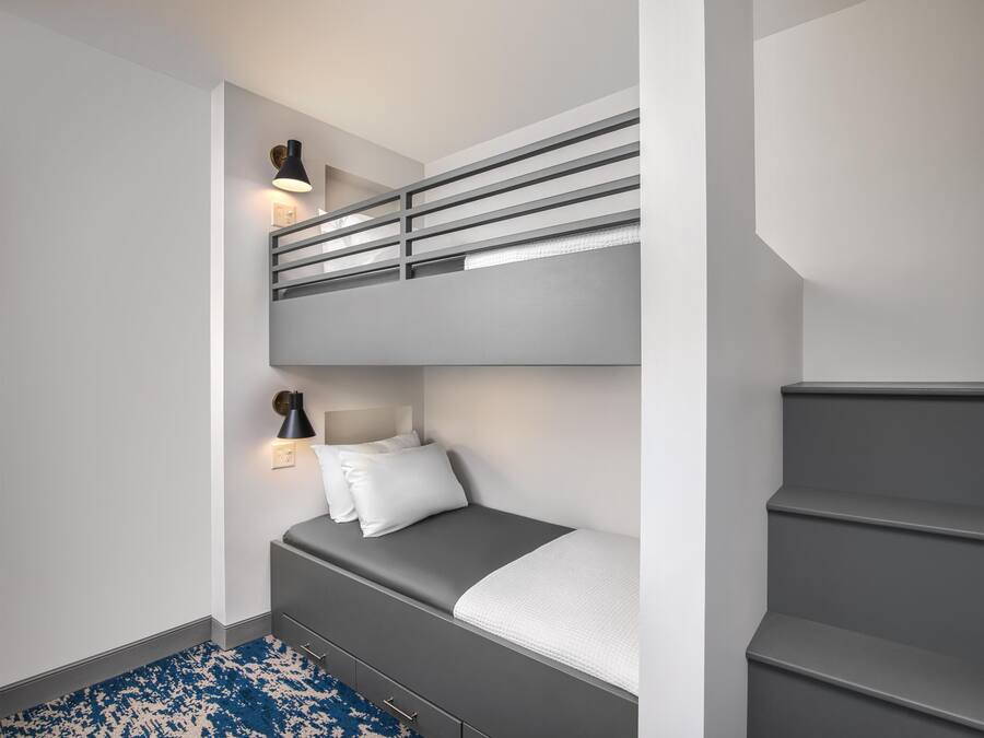 A bunk bed with a desk and chair, a small bedside table with a lamp, and a blue patterned rug.