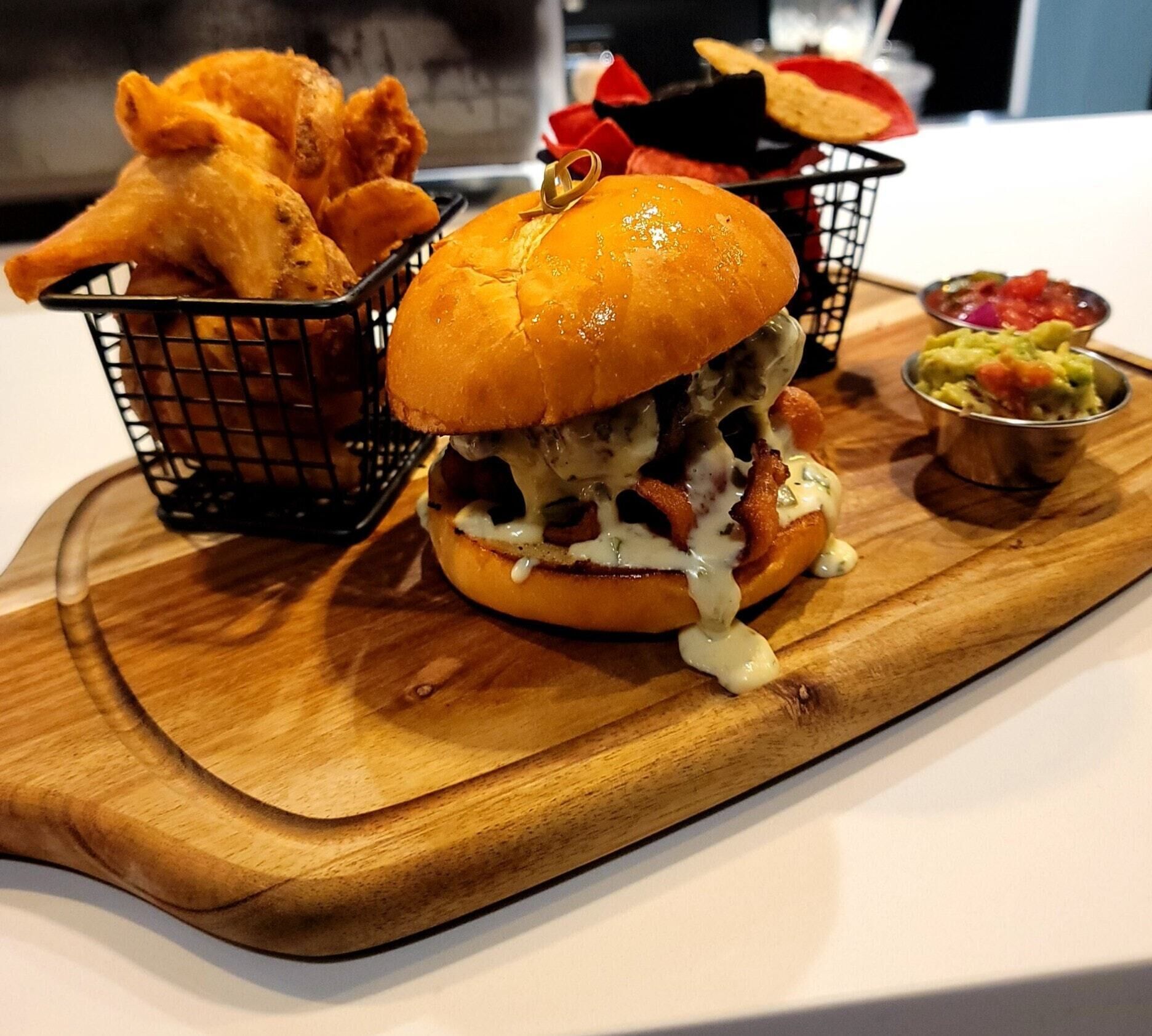 En måltid bestående av en hamburgare, friterad kyckling och guacamole, serverad på en träbricka.