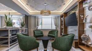 Uma sala de estar moderna com poltronas estofadas em verde, uma mesa redonda e um candelabro.