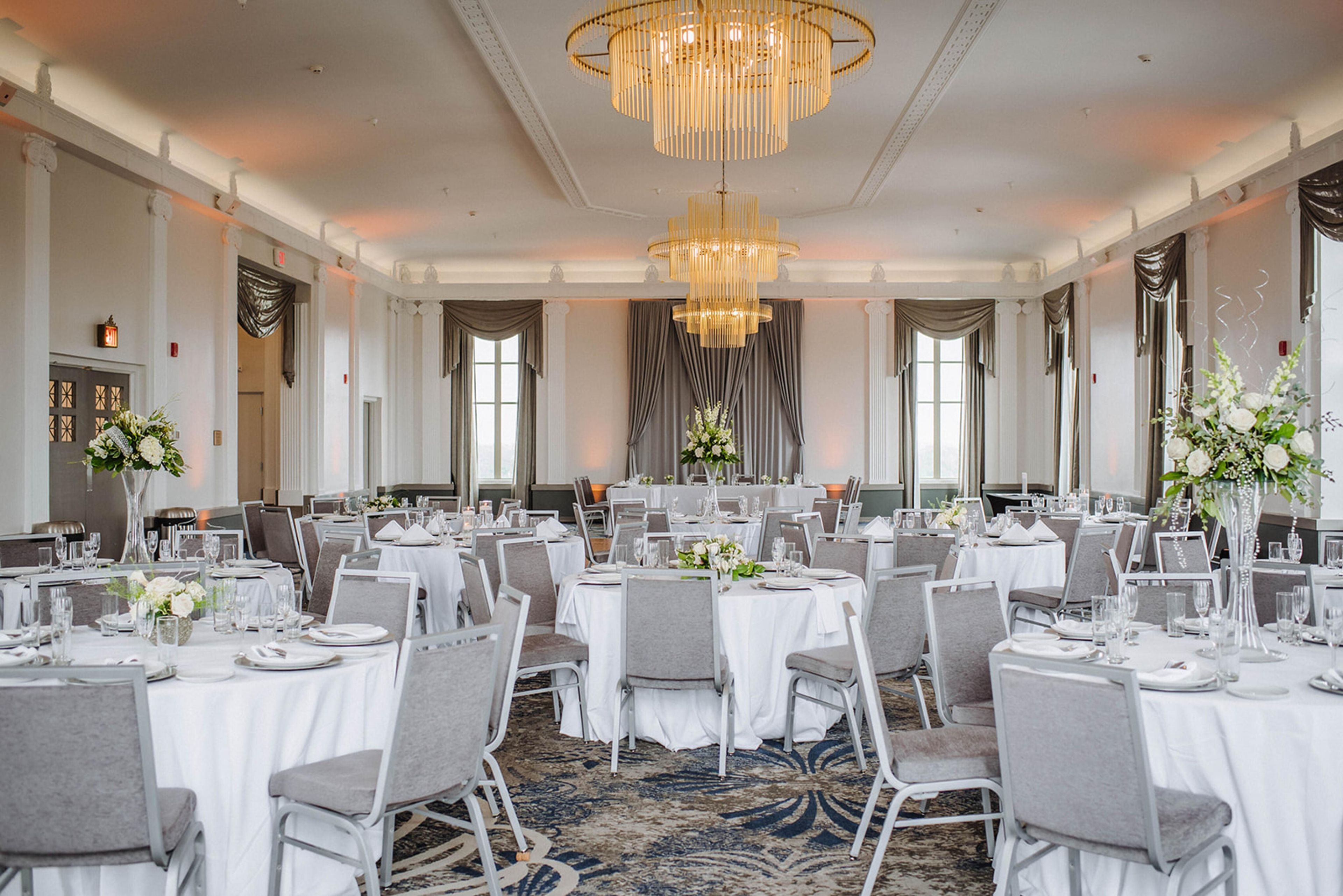 Ein Bankettsaal mit runden Tischen, Stühlen und einer großen Chandelier.