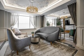 A modern living room with a grey armchair, a patterned armchair, a round coffee table, and a large window with curtains. - Hotel Elkhart, Tapestry Collection by Hilton (Elkhart)