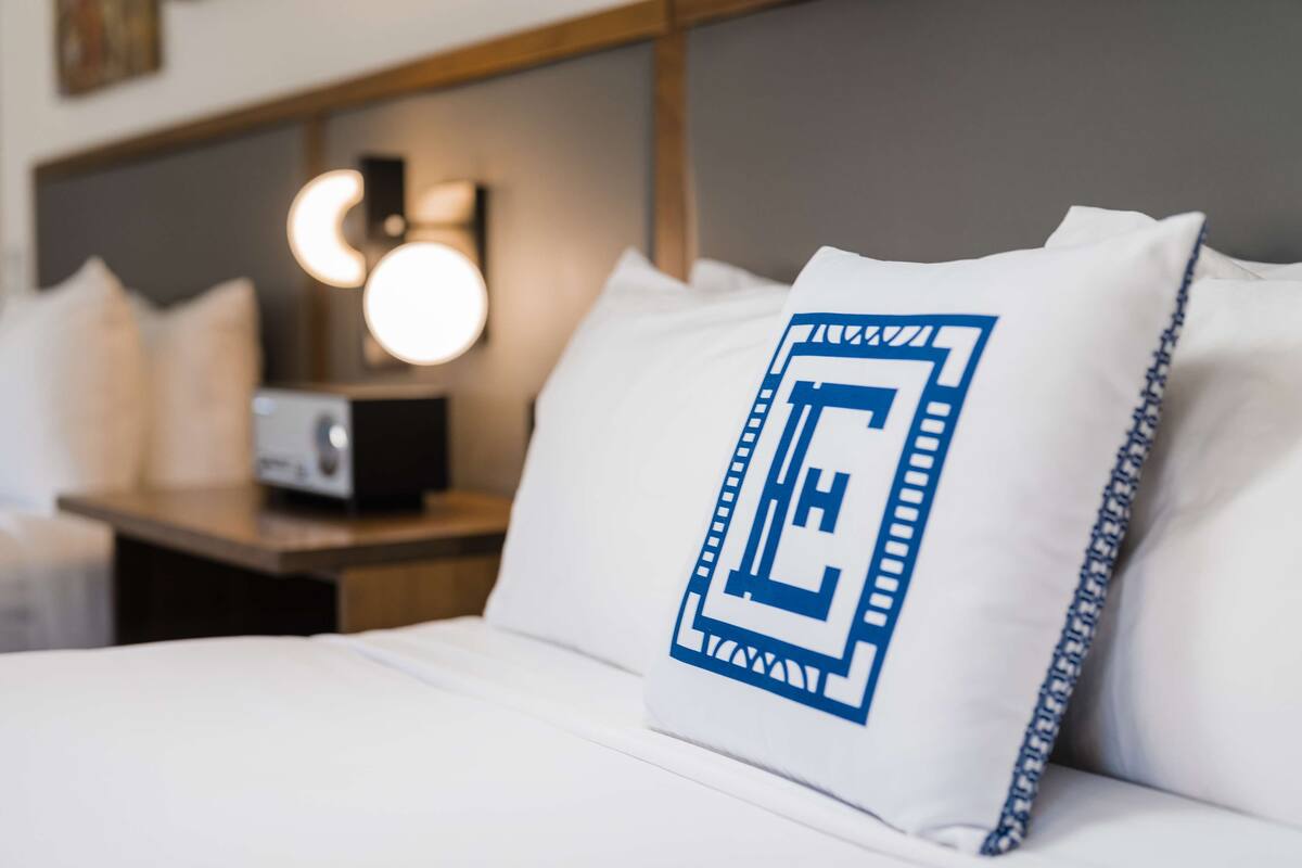 A neatly made bed with white bedding and a pillow featuring a blue design.