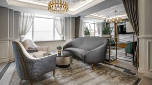 Uma sala de estar moderna com um sofá cinzento, uma poltrona estampada e uma mesa de centro redonda.