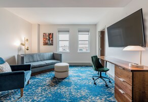 Ein modernes Hotelzimmer mit einem grauen Sofa, einem blauen Sessel, einem Holztisch und einem großen Fernseher.