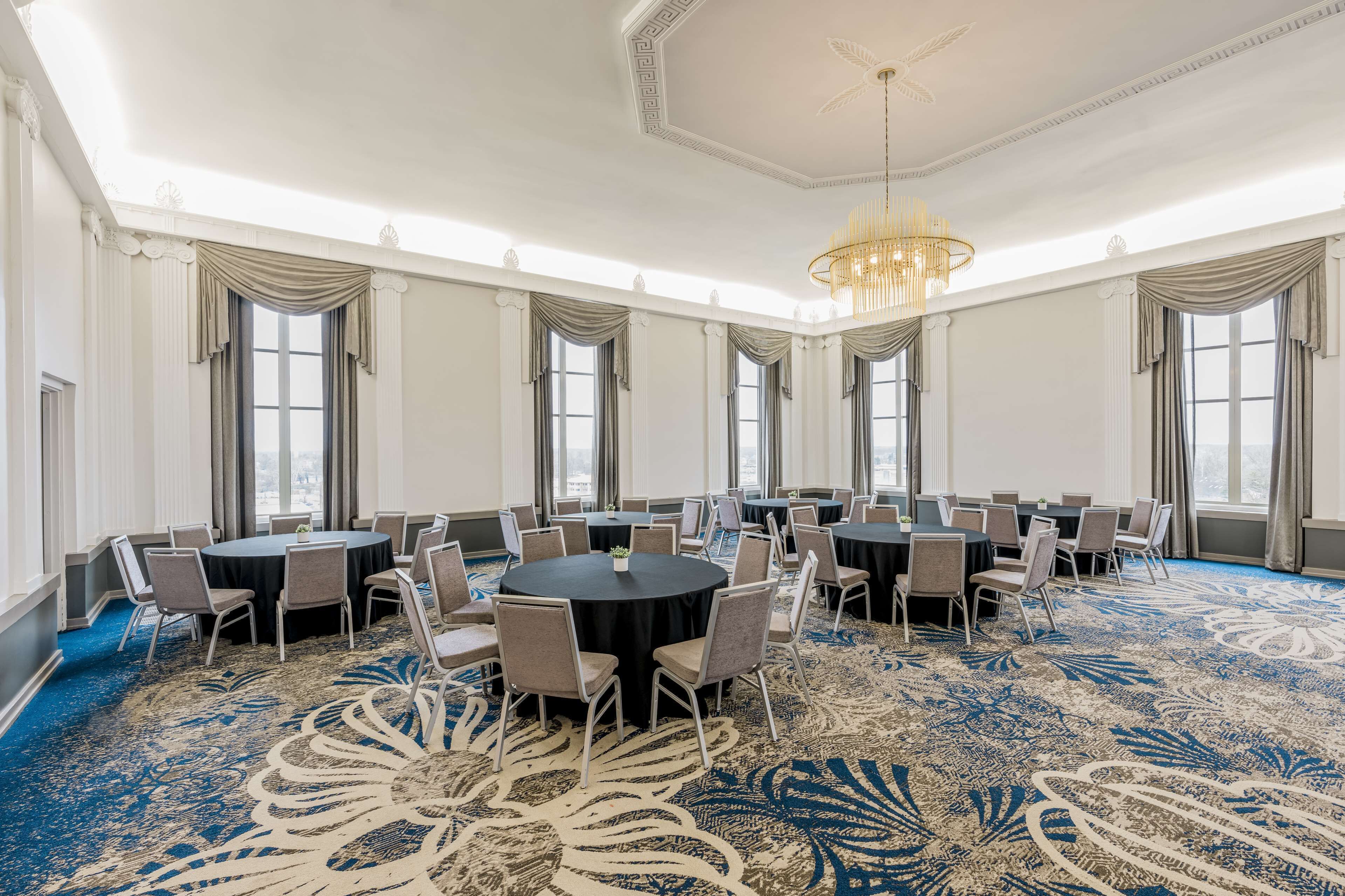A large conference room with round tables and chairs, a patterned carpet, and large windows with curtains.