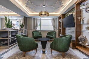 A modern living room with green upholstered chairs, a round coffee table, and a large window with curtains. - Hotel Elkhart, Tapestry Collection by Hilton (Elkhart)