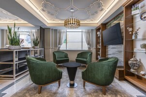 A modern living room with green upholstered chairs, a round coffee table, and a large window with curtains.