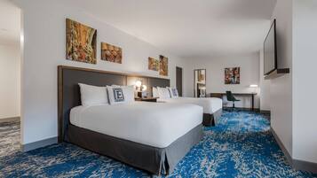 Una habitación de hotel con dos camas, un escritorio, una silla y obras de arte en las paredes.