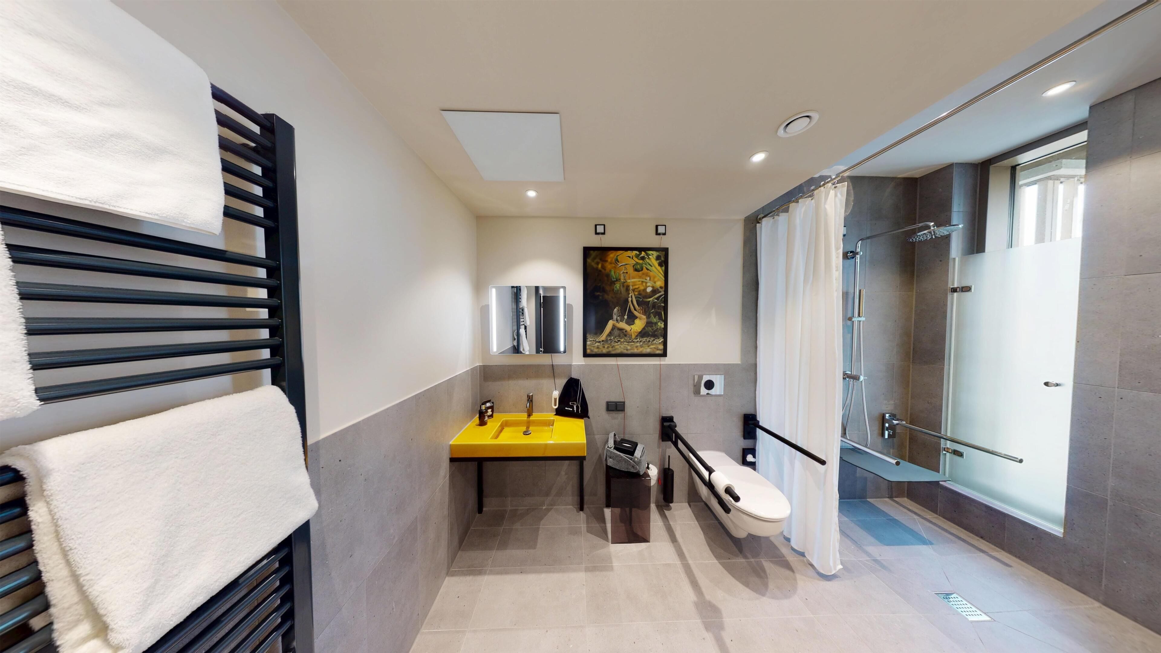 Een moderne badkamer met een geel wastafelmeubel, een douchecabine met glazen wanden en een handdoekrek met witte handdoeken.