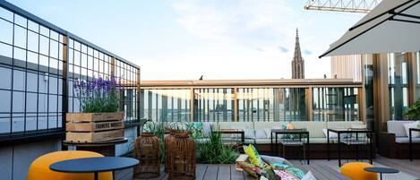Une terrasse sur le toit, dotée d’une plateforme en bois, d’espaces aménagés pour s’asseoir et offrant une vue sur le panorama urbain.