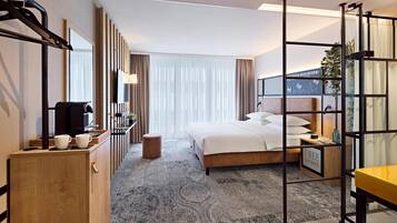 A hotel room with a bed, a desk, a chair, a small table, a cabinet, and a mirror.