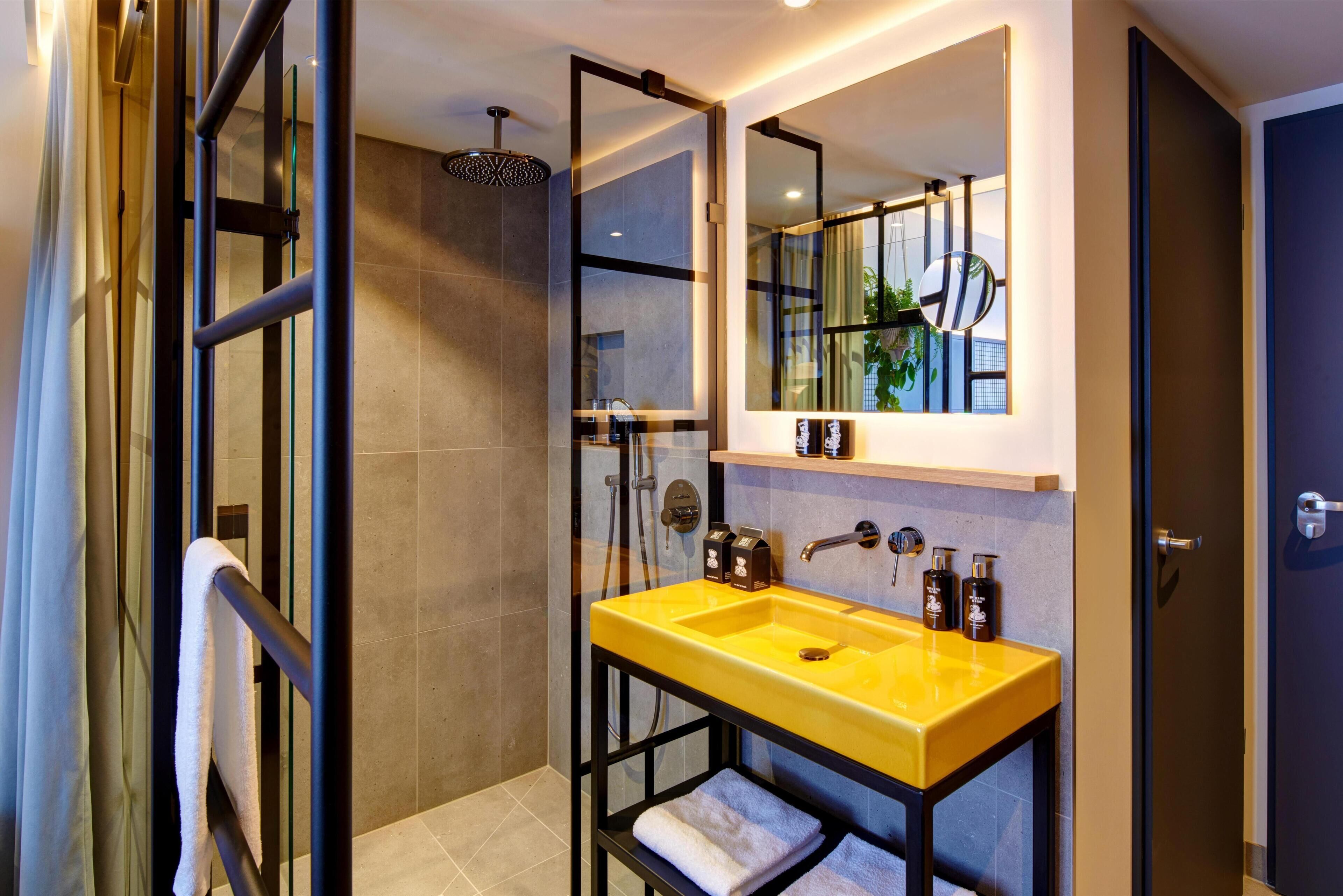 Un baño moderno con cabina de ducha de vidrio, un lavabo amarillo y un espejo grande.