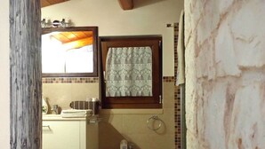 A bathroom with a sink, bidet, and a window with a patterned curtain. - Trullo Degli Ulivi (Castellana Grotte)