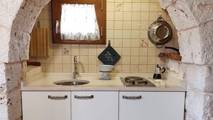 A kitchen with a stone archway, a window with a lace curtain, a sink, a stove, and cabinets. - Trullo Degli Ulivi (Castellana Grotte)