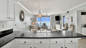 Una cocina amplia con una isla grande, armarios blancos y vista al área de estar.
