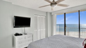 Un dormitorio con cama, televisión, cómoda y balcón con vista al océano.
