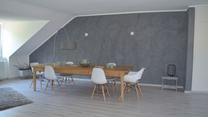 A dining area with a wooden table and white chairs, a grey textured wall, and a small side table with a lamp. - 2.5 room apartment in central forest location Essen-Bredeney/Rüttenscheid (Essen)