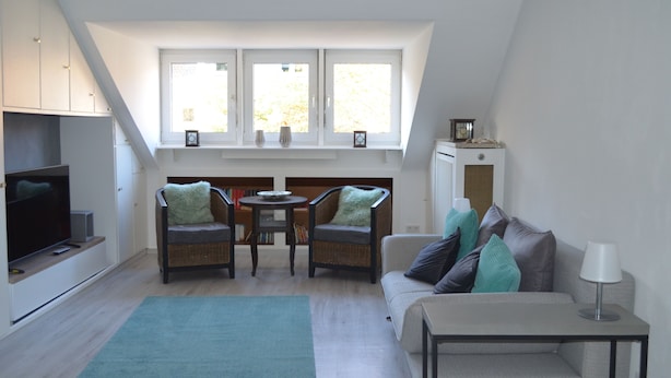 A modern living room with a television, two chairs, a sofa, a small table, and a window with a view. - 2.5 room apartment in central forest location Essen-Bredeney/Rüttenscheid (Essen)