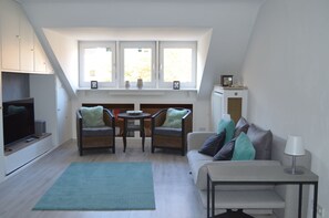A modern living room with a television, two chairs, a sofa, a small table, and a window with a view. - 2.5 room apartment in central forest location Essen-Bredeney/Rüttenscheid (Essen)