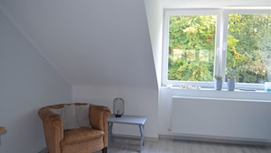 A room with a sloped ceiling, a brown leather armchair, a small table with a lamp, and a window with a view of trees. - 2.5 room apartment in central forest location Essen-Bredeney/Rüttenscheid (Essen)