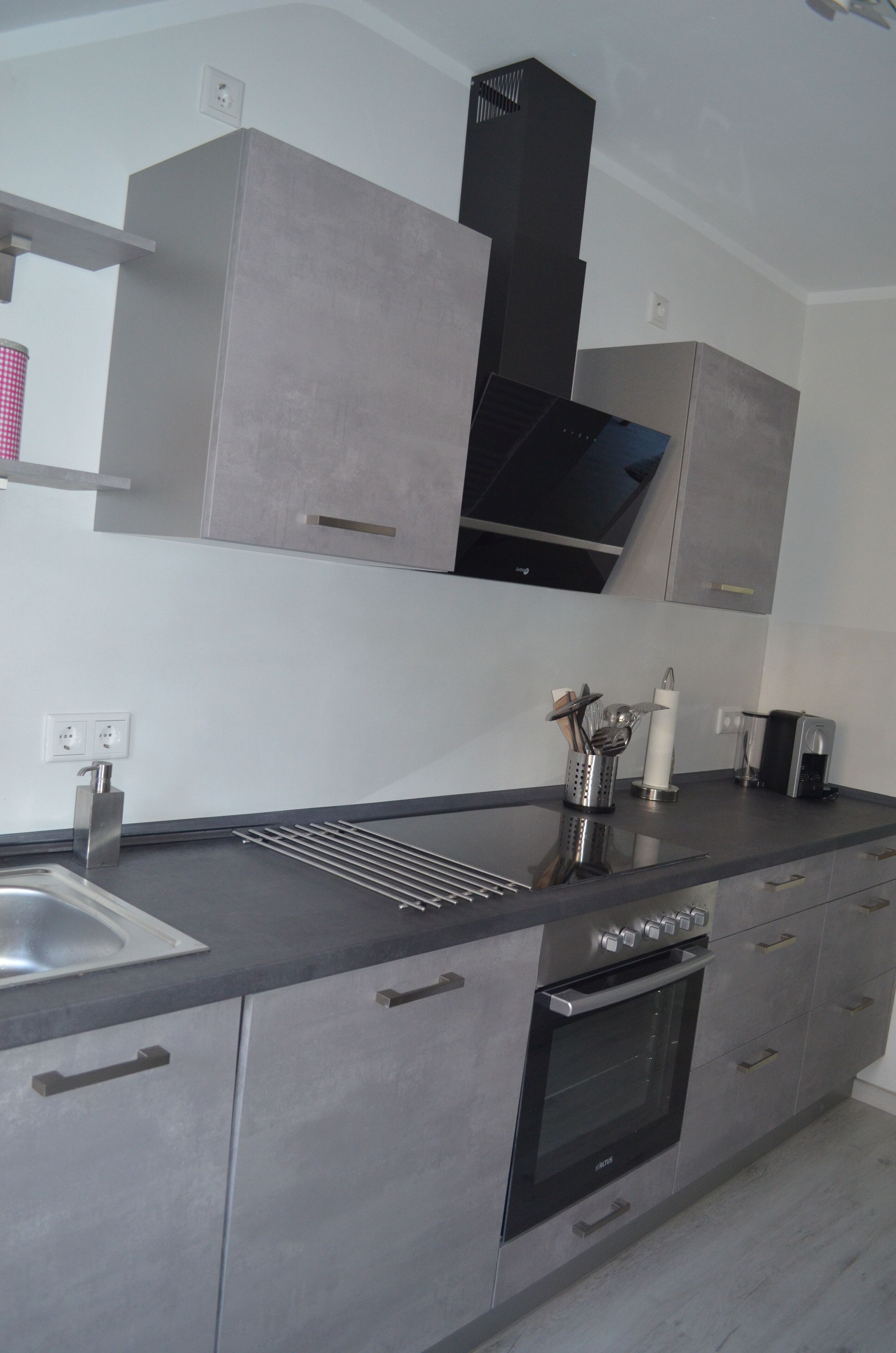 A modern kitchen with grey cabinets, a stainless steel sink, and a built-in oven.