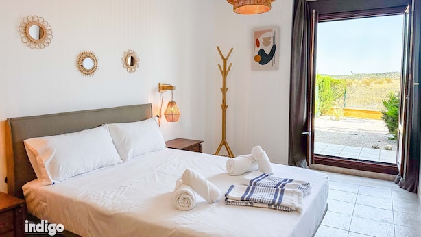 A hotel room with a large bed, a bedside table, a wall-mounted lamp, decorative mirrors, and a view of the outdoors.