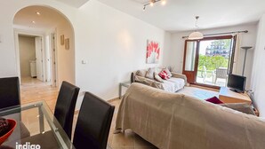Ein modernes Wohnzimmer mit einer Couch, einem Fernseher und einem Essbereich mit Stühlen und einem Glastisch.