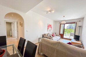 A modern living room with a sofa, a TV, and a dining area with chairs and a glass table.