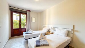 A hotel room with two beds, a small table, and a window with curtains. - Apartment with garden & direct access to the pool CAP01 (Ayamonte)