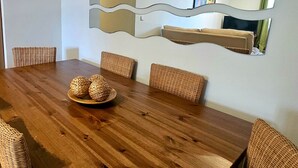 A dining area with a wooden table, wicker chairs, and a decorative mirror with a wavy frame. - Apartment with garden & direct access to the pool CAP01 (Ayamonte)
