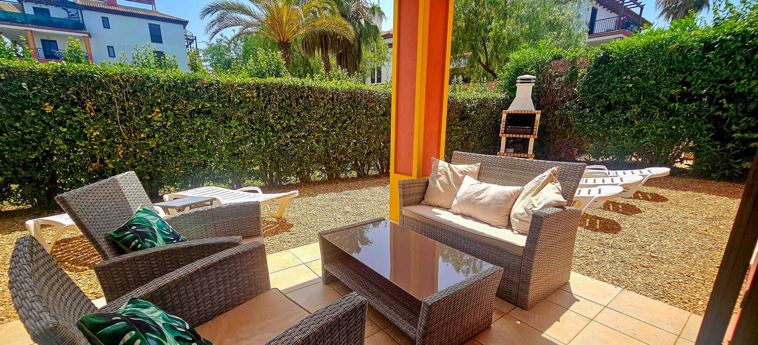 Un espace extérieur aménagé en terrasse, avec des meubles en osier, une table à plateau de verre et un barbecue.